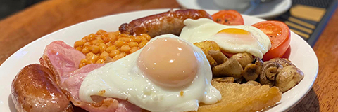 a English breakfast plate of eggs, sausages, mushrooms, bacon, tomatoes and baked beans