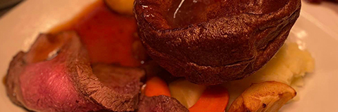 a dinner plate with a rare beef slice and Yorkshire pudding