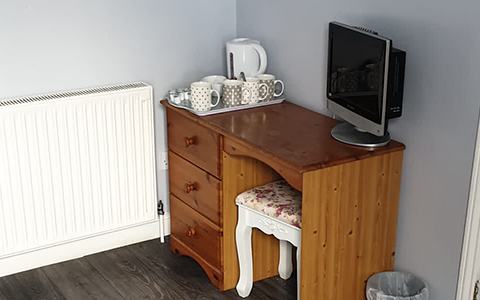 a small desk area with a television, kettle and mugs for making tea